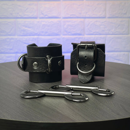 Black leather cuffs with metal hooks on a dark surface