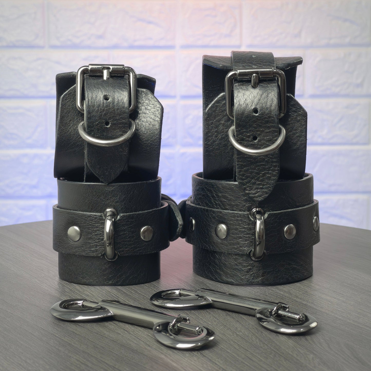 Black leather handcuff and ankle cuffs with silver hardware on a gray surface.