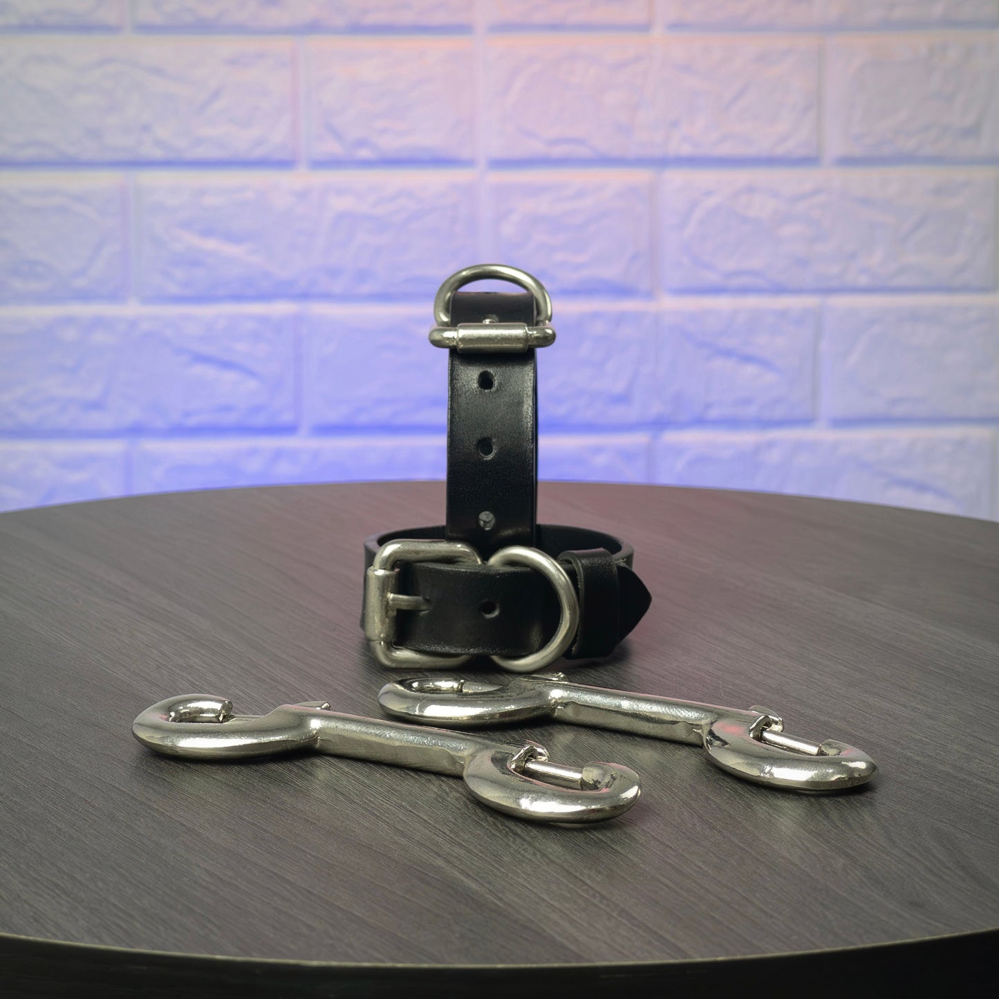 Black leather handcuffs with silver hardware on a wooden surface