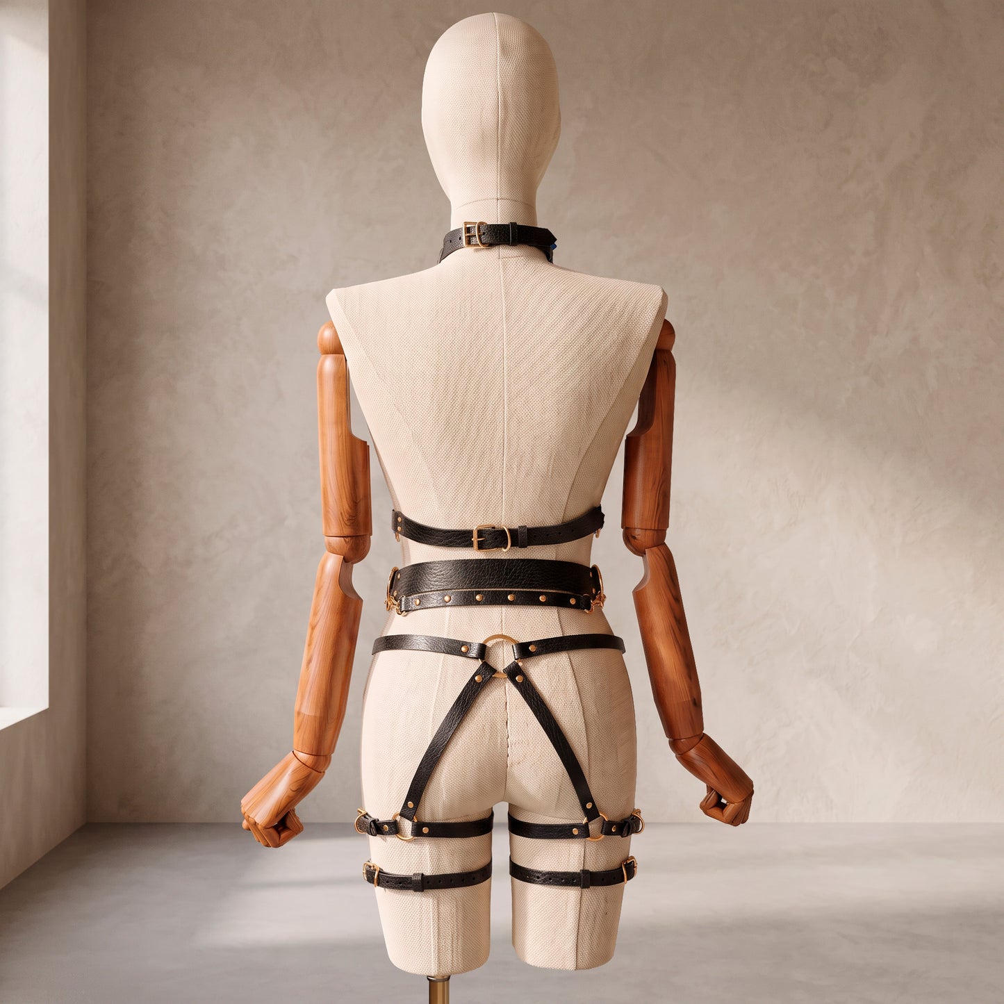 Back view of a deep black leather full body harness set with an open bust harness, open crotch garter belt, removable leather handle, large front ring, adjustable straps, and gold-tone metal hardware.