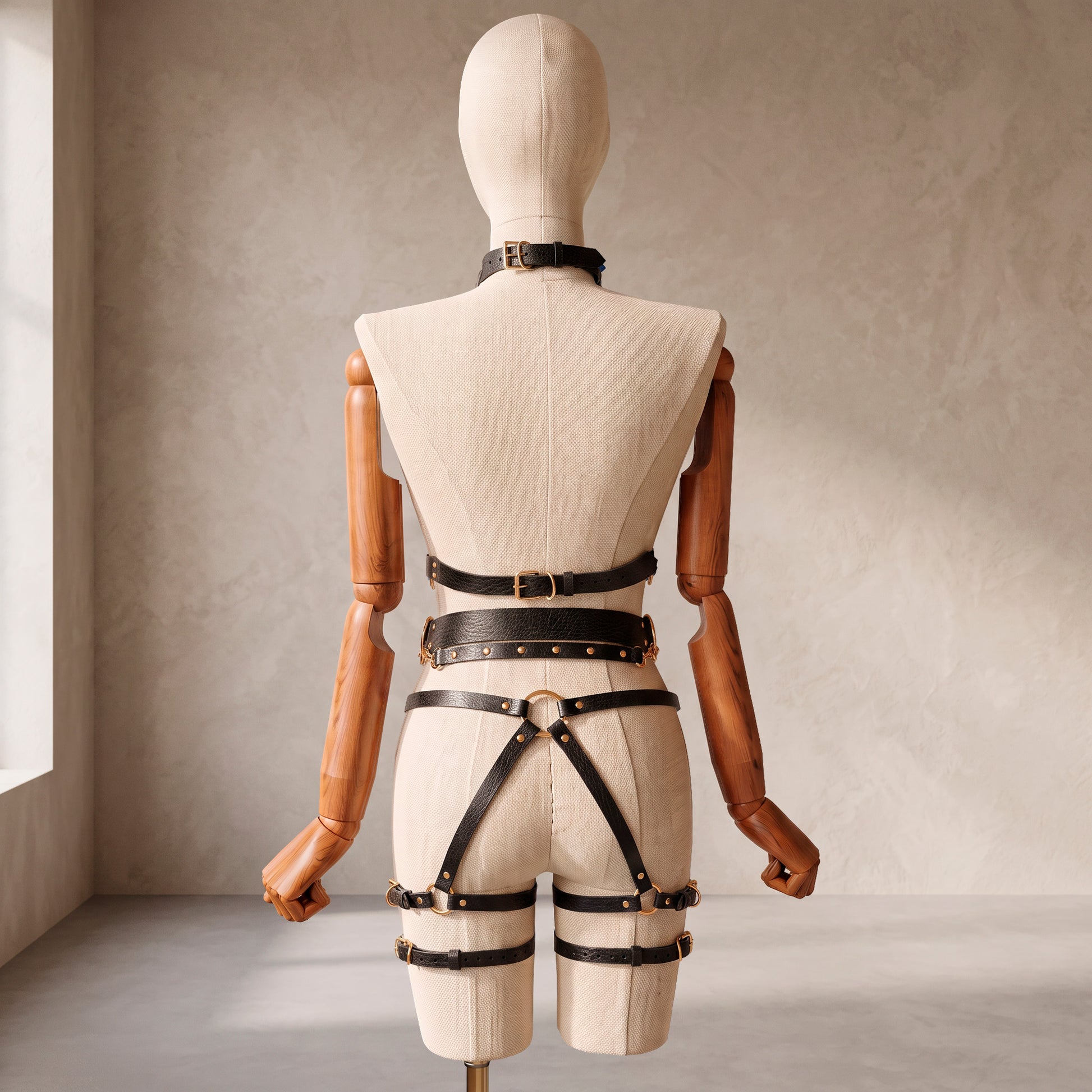 Back view of a deep black leather full body harness set with an open bust harness, open crotch garter belt, removable leather handle, large front ring, adjustable straps, and gold-tone metal hardware.