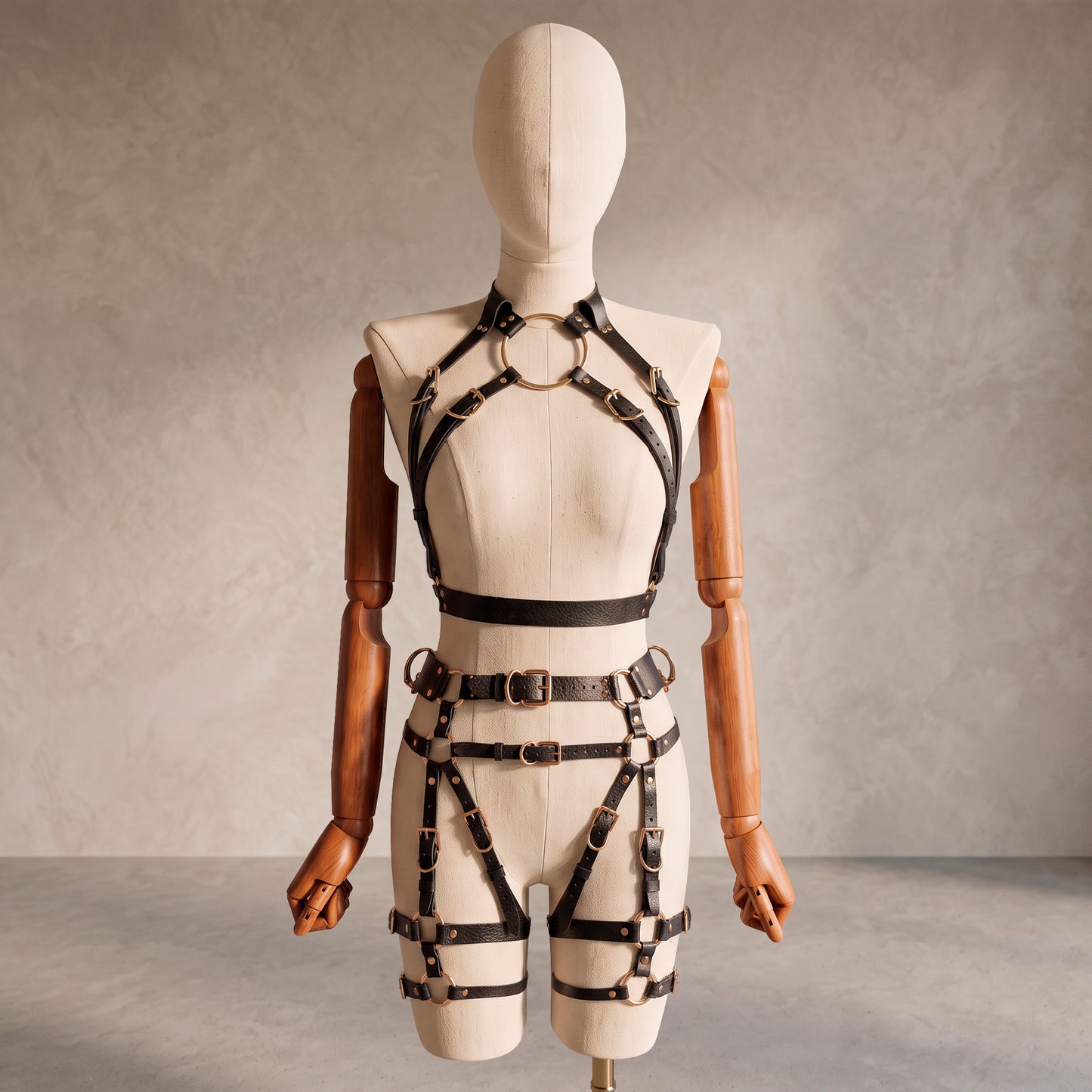 Front view of a deep black leather full body harness set with an open bust harness, open crotch garter belt, removable leather handle, large front ring, adjustable straps, and gold-tone metal hardware.