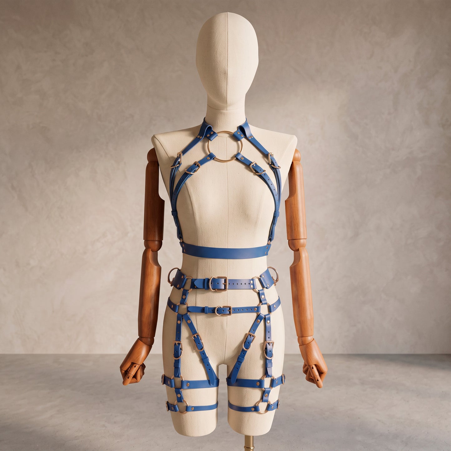 Front view of a deep blue leather full body  harness set with an open bust harness, open crotch garter belt, removable leather handle, large front ring, adjustable straps, and gold-tone metal hardware.
