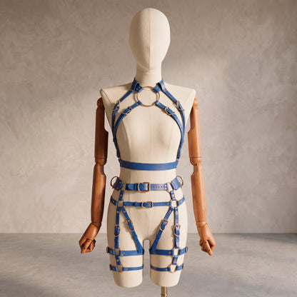 Front view of a deep blue leather full body  harness set with an open bust harness, open crotch garter belt, removable leather handle, large front ring, adjustable straps, and gold-tone metal hardware.