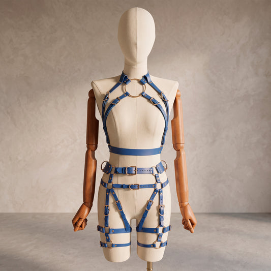 Front view of a deep blue leather full body  harness set with an open bust harness, open crotch garter belt, removable leather handle, large front ring, adjustable straps, and gold-tone metal hardware.