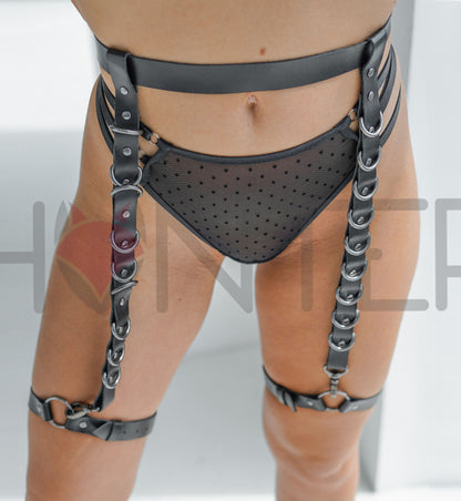 Black genuine leather thigh harness belt, close-up detail of dark nickel D-rings and riveted strap construction showing the loop section where the waist belt threads through the vertical strap.