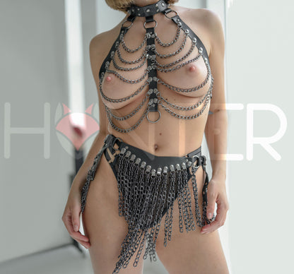 Front view of a black leather festival set with dark nickel hardware, showing a chain drape chest harness with a high collar, layered suspended chains across the chest, and a chain skirt belt with a large front chain panel and side draped chain sections.