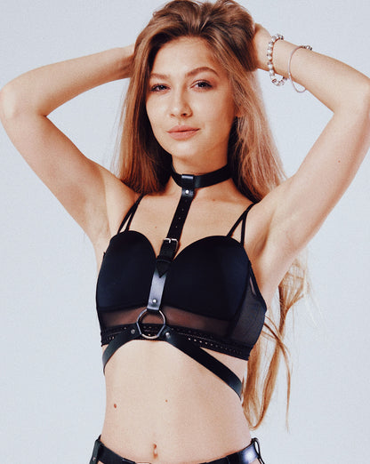 Black genuine leather minimalist O-ring harness with dark nickel ring and buckles, three-quarter front view on model showing alignment from 3/4 inch (2 cm) choker to central O-ring and 3/4 inch (2 cm) waist belt; leather thickness 1.4–1.8 mm.