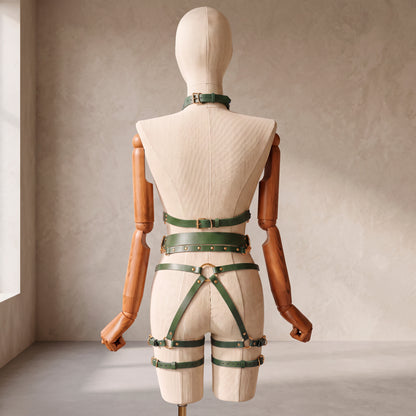 Back view of a deep green leather full body harness set with an open bust harness, open crotch garter belt, removable leather handle, large front ring, adjustable straps, and gold-tone metal hardware.