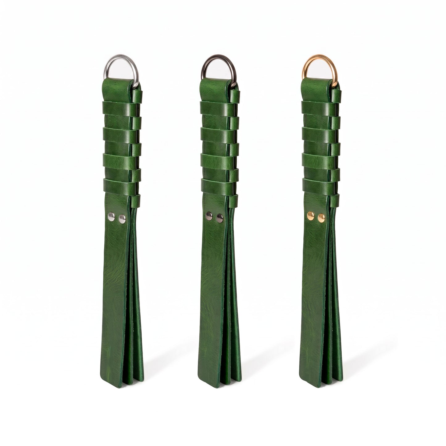Three dark green leather flogger-style accessories with woven strap sections and metal rings, displayed side by side on a white background. Hardware in Silver, Dark nickel and gold colors.