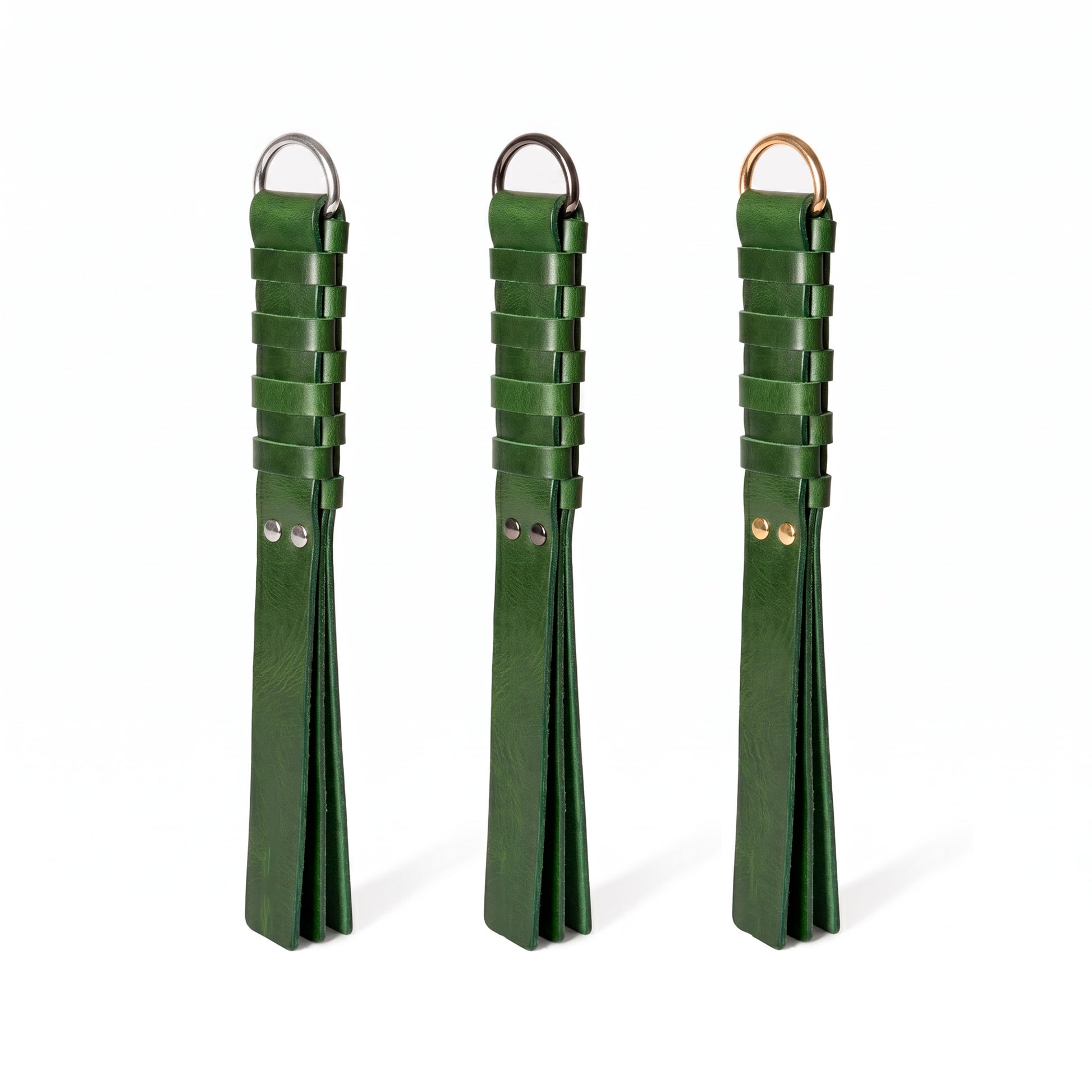 Three dark green leather flogger-style accessories with woven strap sections and metal rings, displayed side by side on a white background. Hardware in Silver, Dark nickel and gold colors.