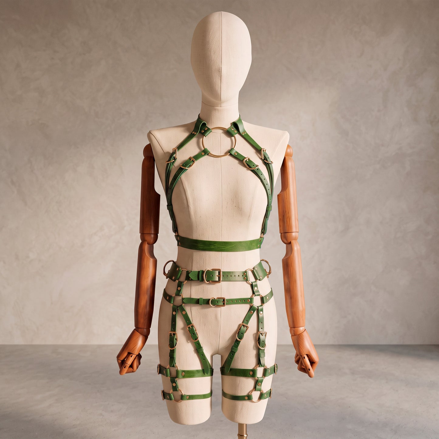 Front view of a deep green leather full body harness set with an open bust harness, open crotch garter belt, removable leather handle, large front ring, adjustable straps, and gold-tone metal hardware.