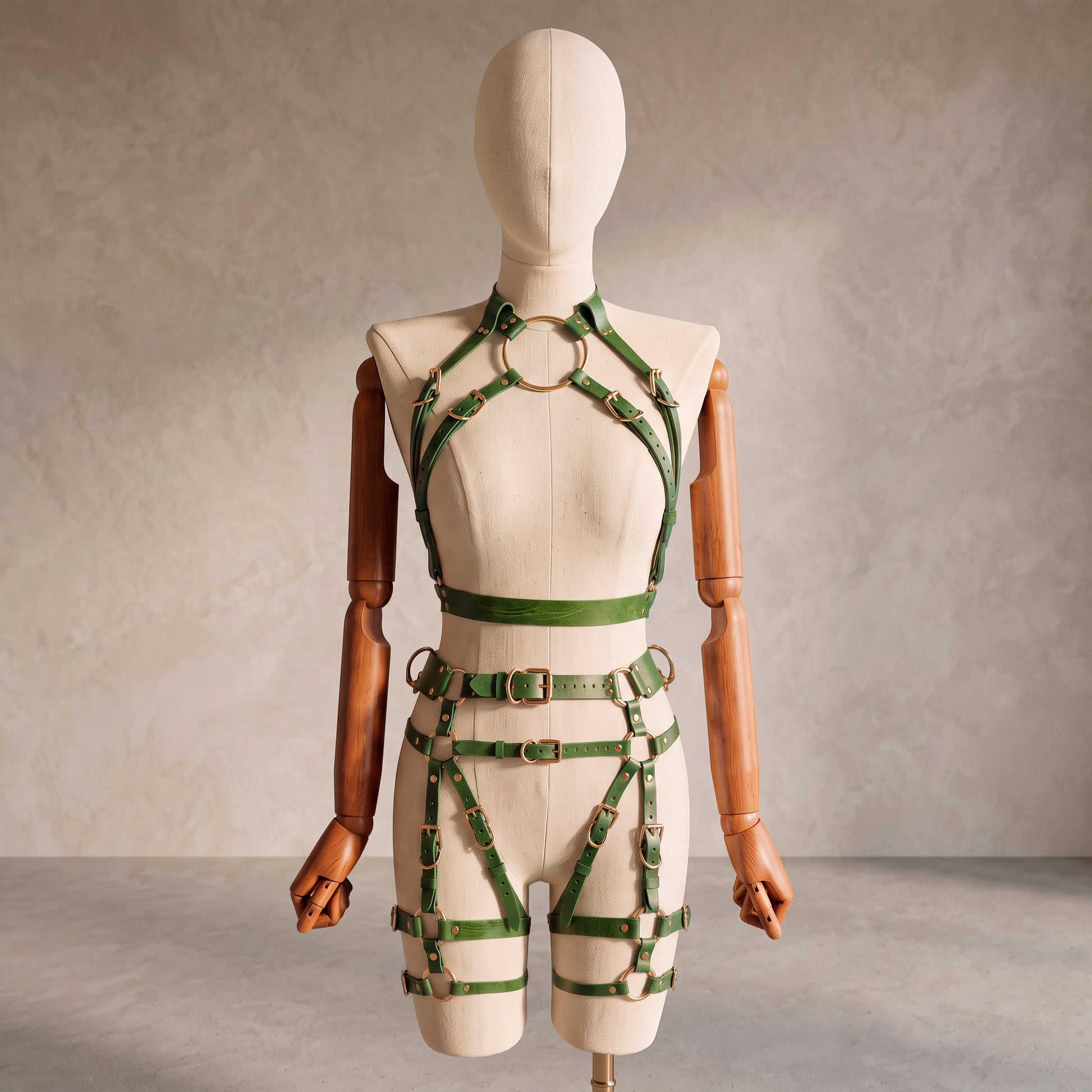 Front view of a deep green leather full body harness set with an open bust harness, open crotch garter belt, removable leather handle, large front ring, adjustable straps, and gold-tone metal hardware.