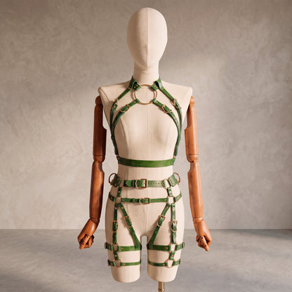 Front view of a deep green leather full body harness set with an open bust harness, open crotch garter belt, removable leather handle, large front ring, adjustable straps, and gold-tone metal hardware.