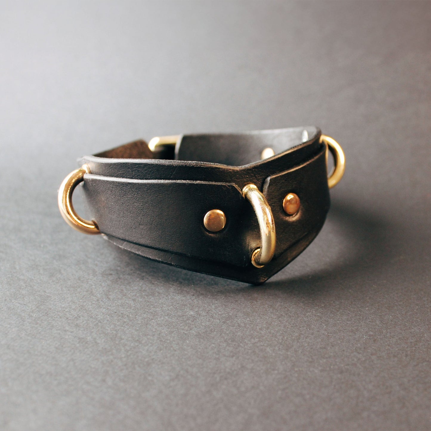 Black leather collar with gold hardware on a gray background
