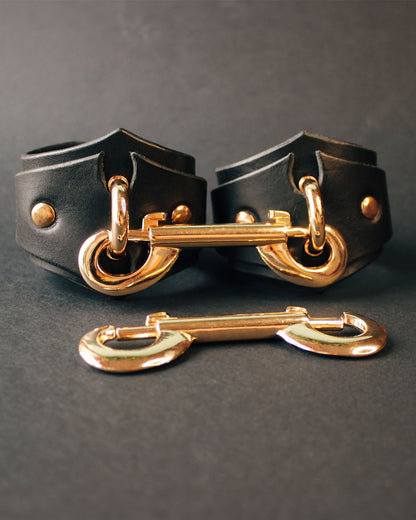 Black leather handcuffs with gold hardware on a dark gray background