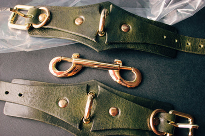 Green leather handcuffs with gold hardware on a dark surface