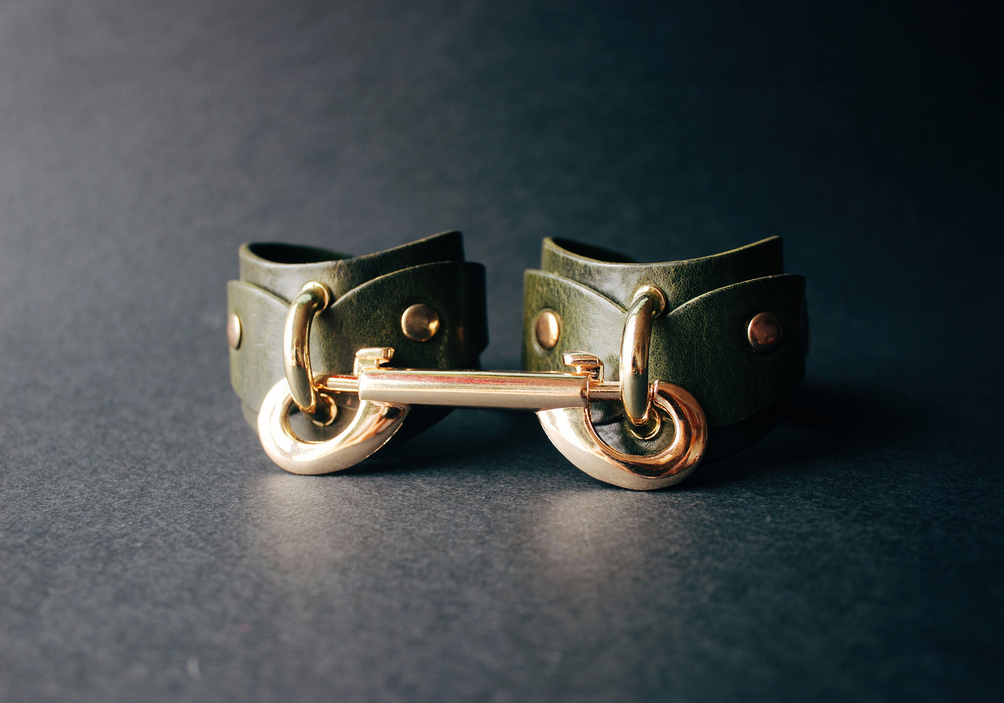 Green leather cuffs with gold hardware on a dark background