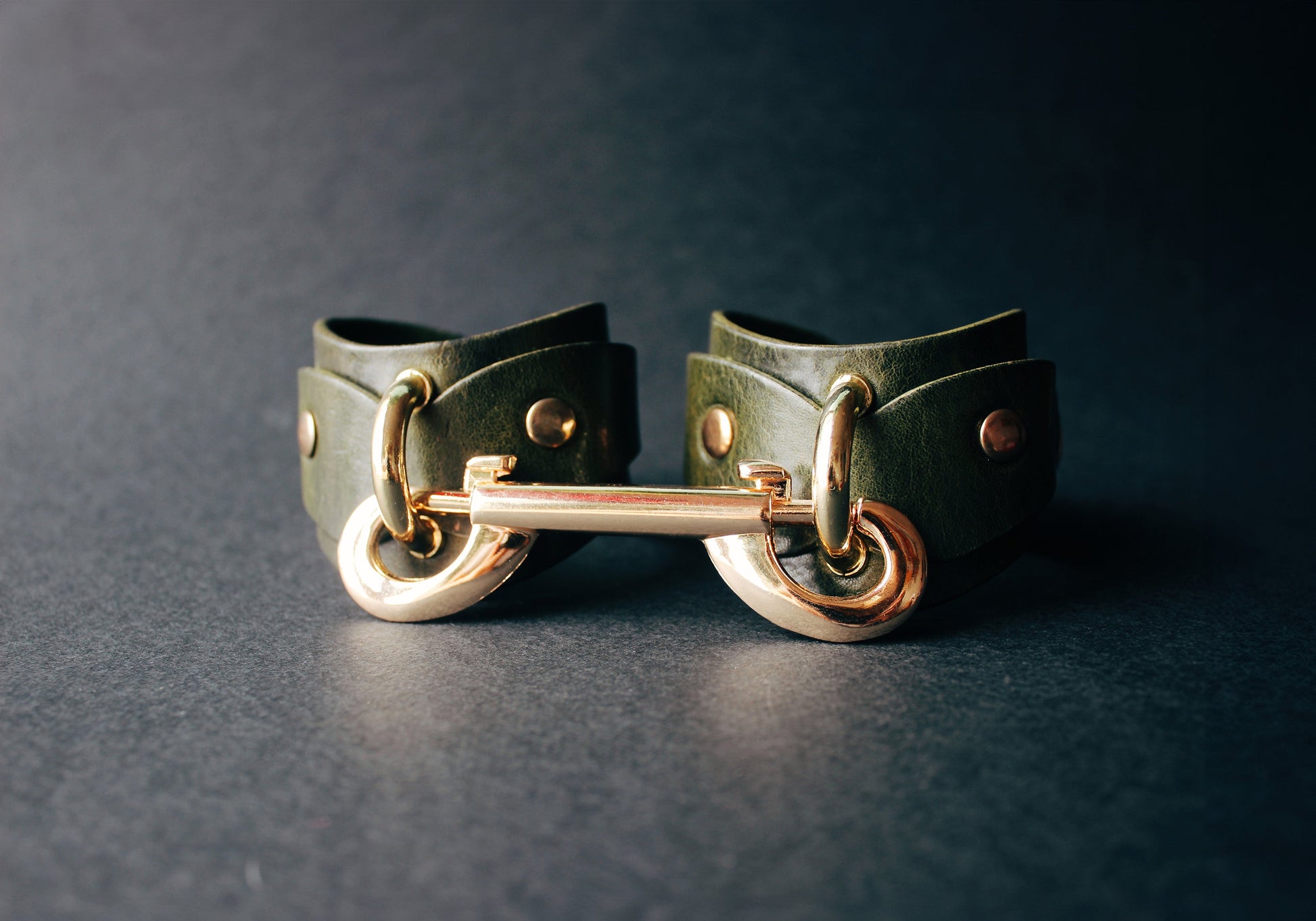 Green leather cuffs with gold hardware on a dark background
