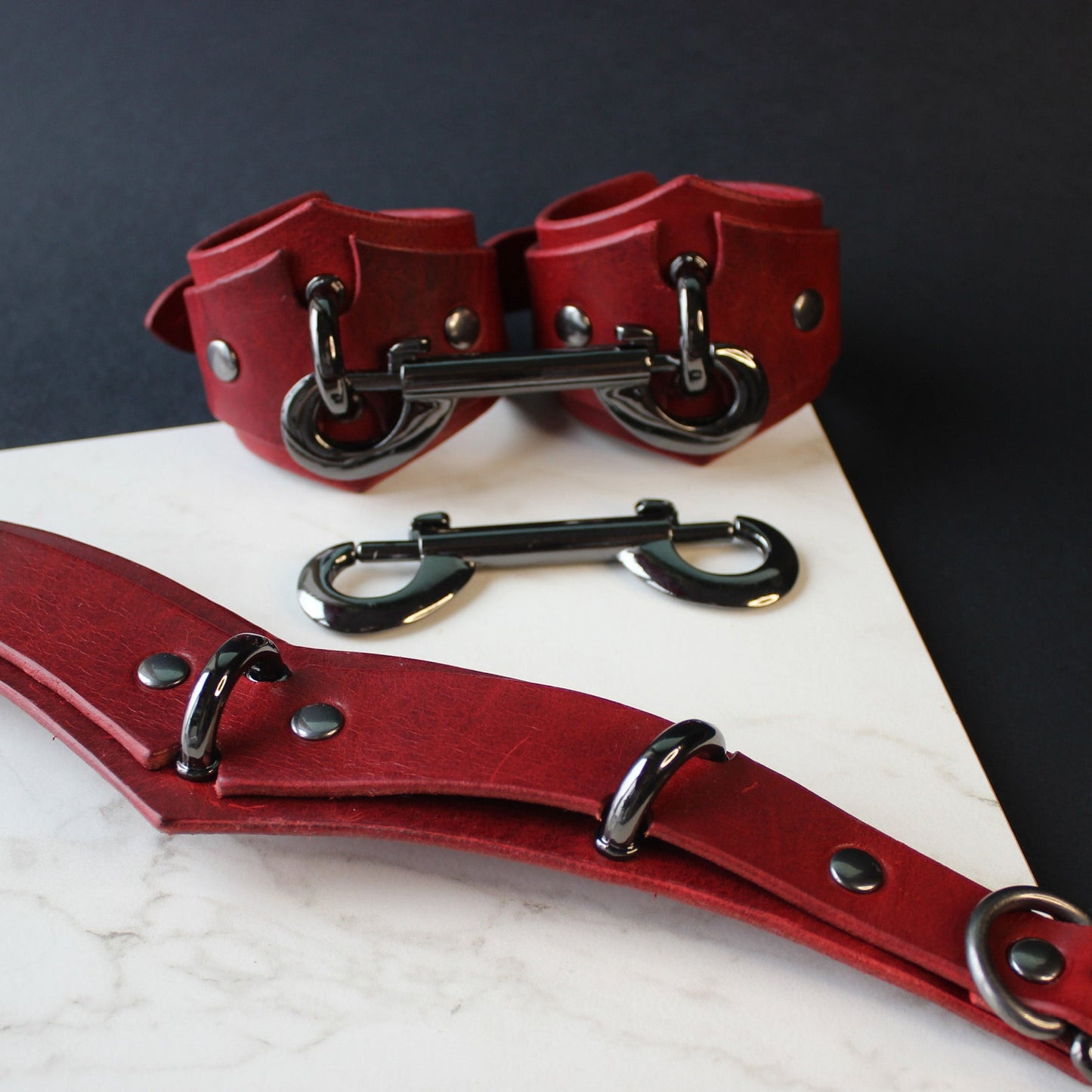 Red leather collar and cuffs set on a dark surface