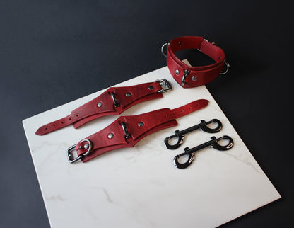 Red leather collars and cuffs on a white surface with a dark background