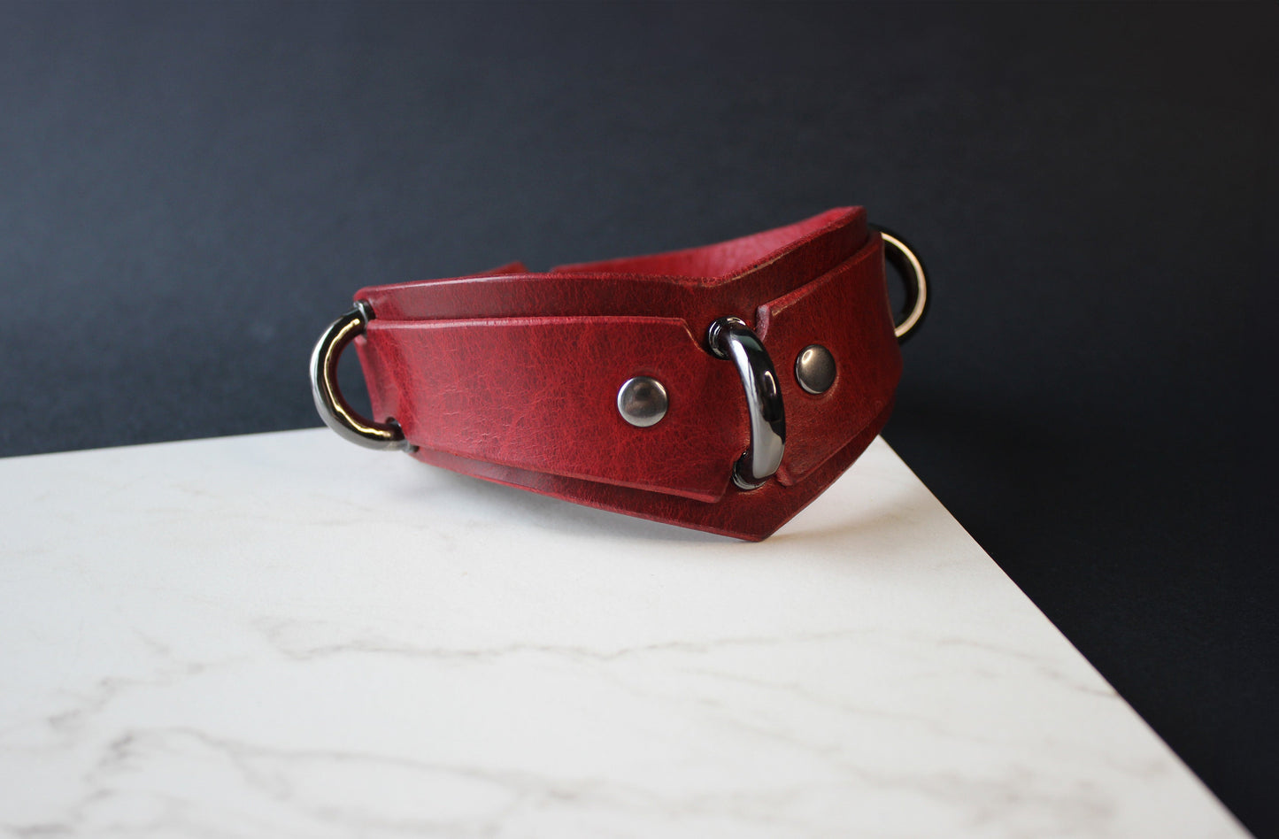 Red leather collar with metal rings on a white surface and dark background