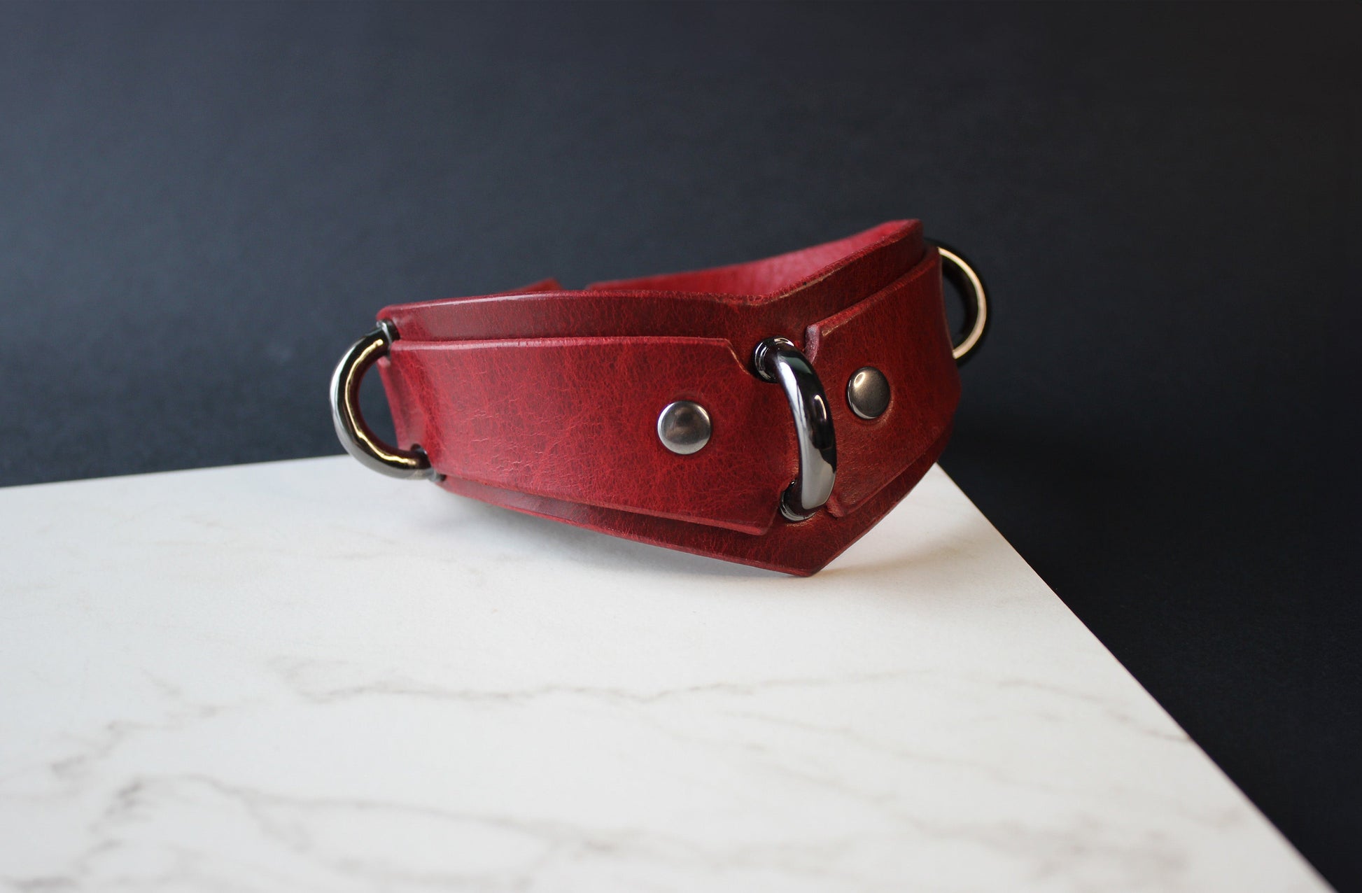 Red leather collar with metal rings on a white surface and dark background