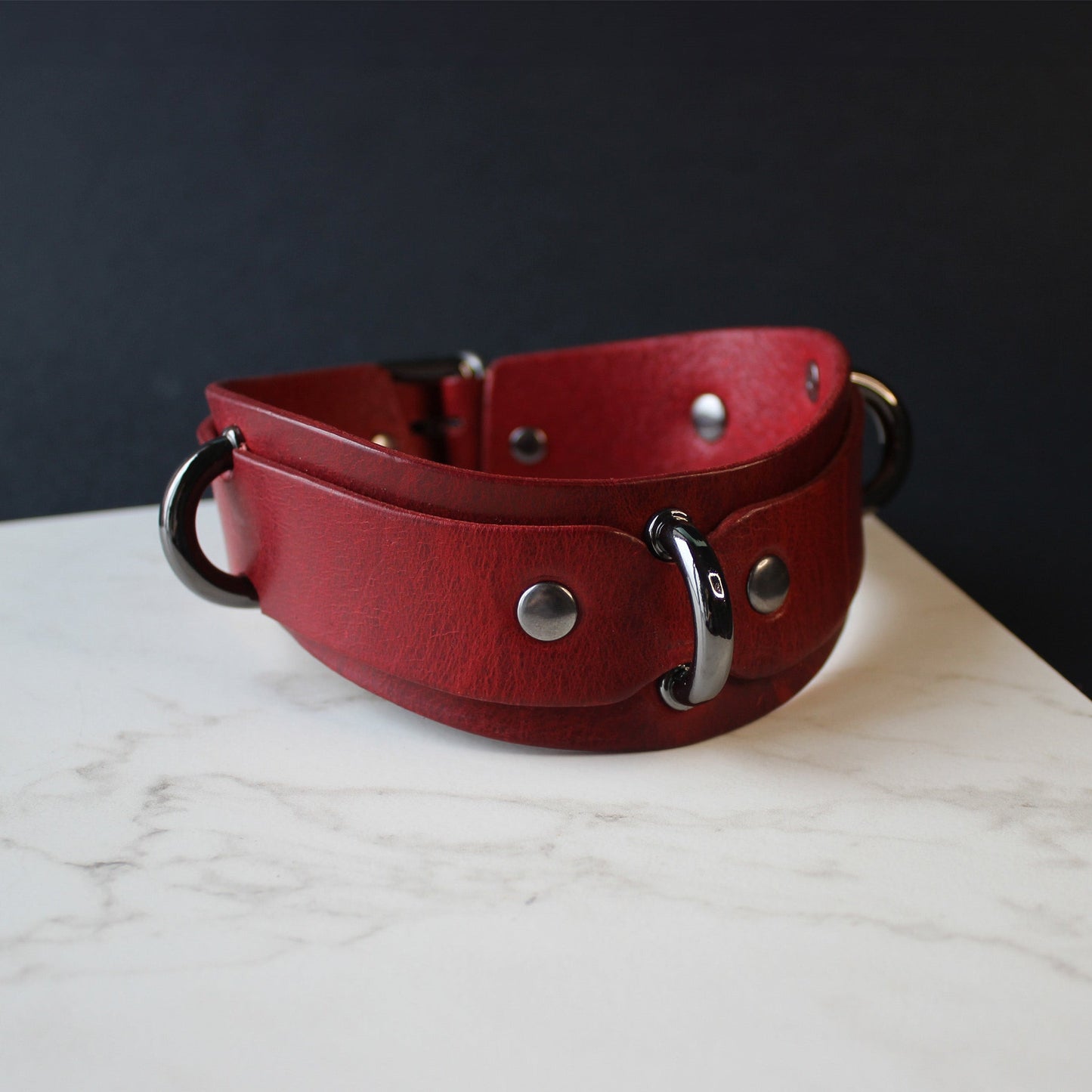Red leather collar with black hardware on a marble surface with a dark background