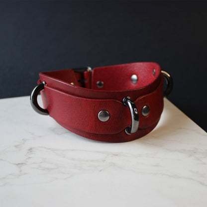 Red leather collar with black hardware on a marble surface with a dark background