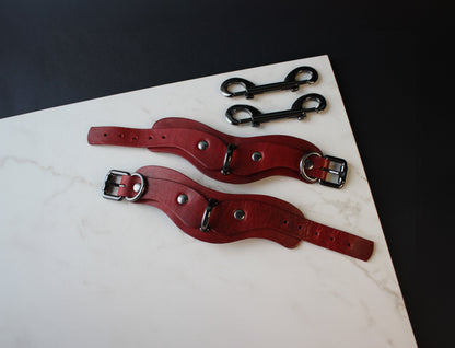 Two red leather handcuffs with metal buckles on a marble surface.
