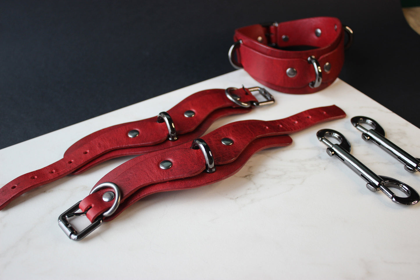Red leather collar and cuffs with metal hardware on a white surface.