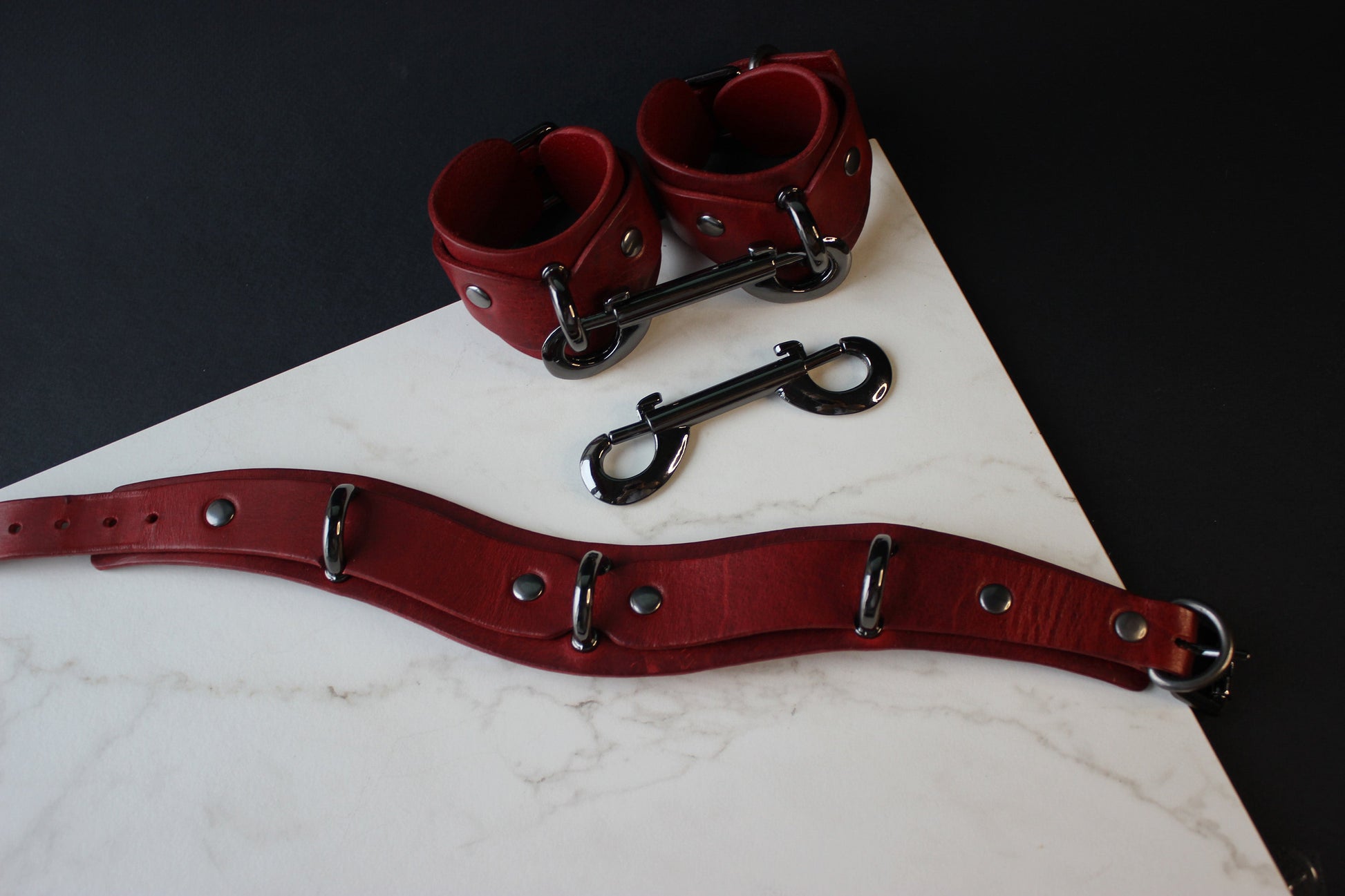 Red leather collar and cuffs with metal hardware on a white marble surface.
