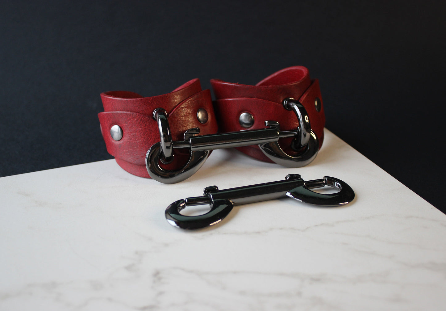Red leather handcuffs with black hardware on a marble surface
