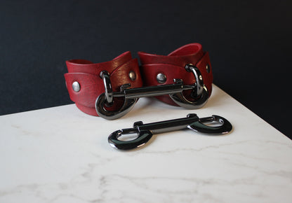 Red leather handcuffs with black hardware on a marble surface