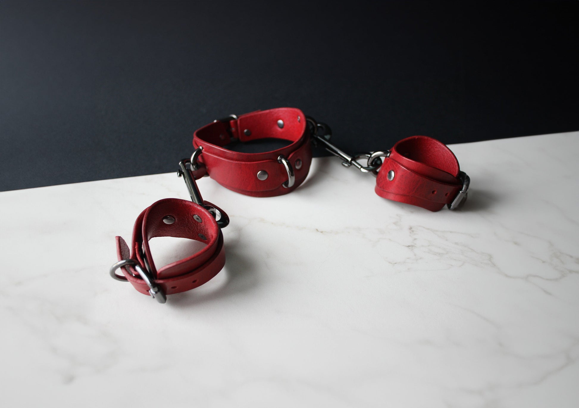 Red leather handcuffs on a white surface with a dark background