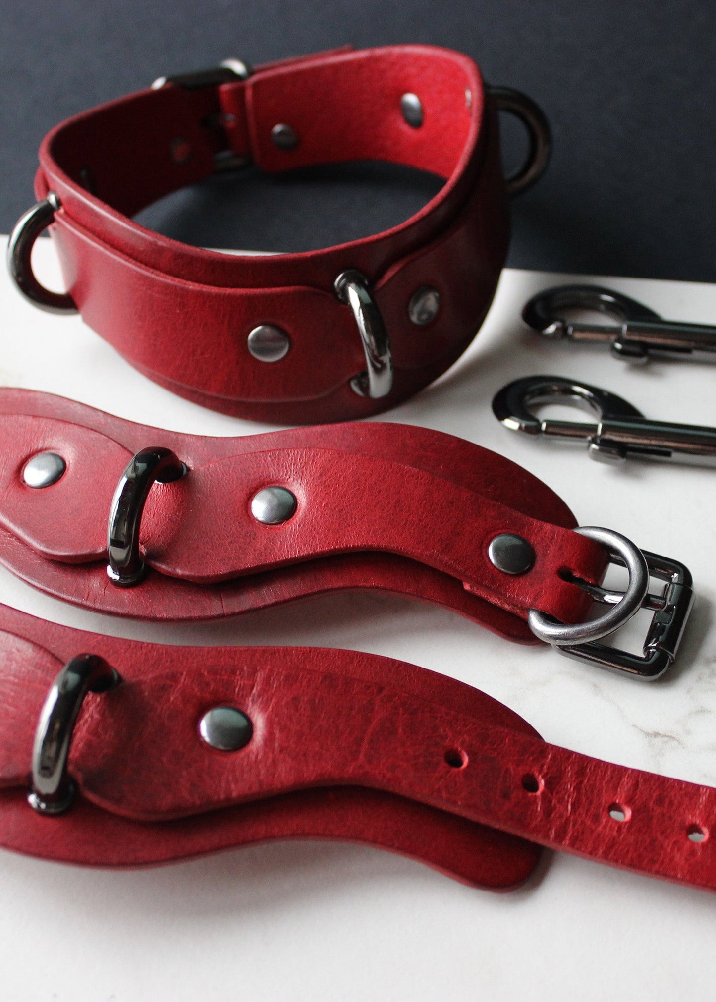 Red leather collars and cuffs on a white surface with a dark background