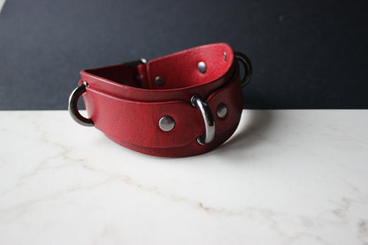 Red leather collar with metal hardware on a white surface and dark background