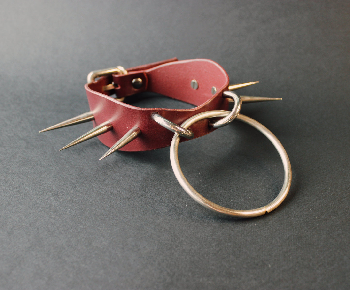 Marsala leather collar with spikes and a metal ring on a gray background