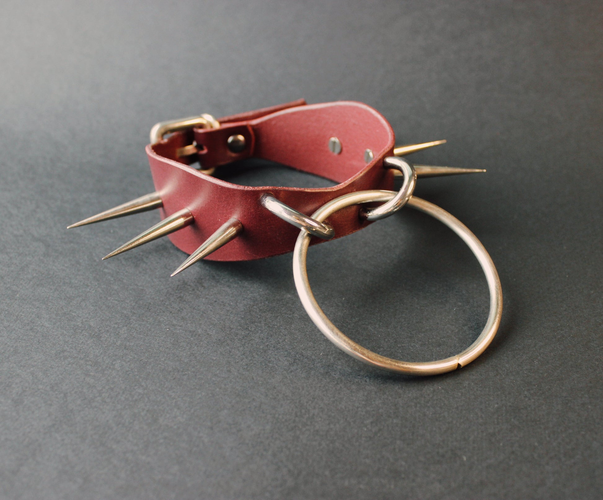 Marsala leather collar with spikes and a metal ring on a gray background