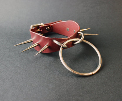 Marsala leather collar with spikes and a metal ring on a gray background