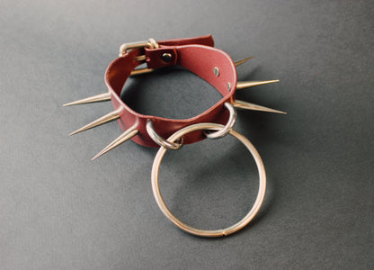 Marsala leather collar with spikes and a metal ring on a gray background
