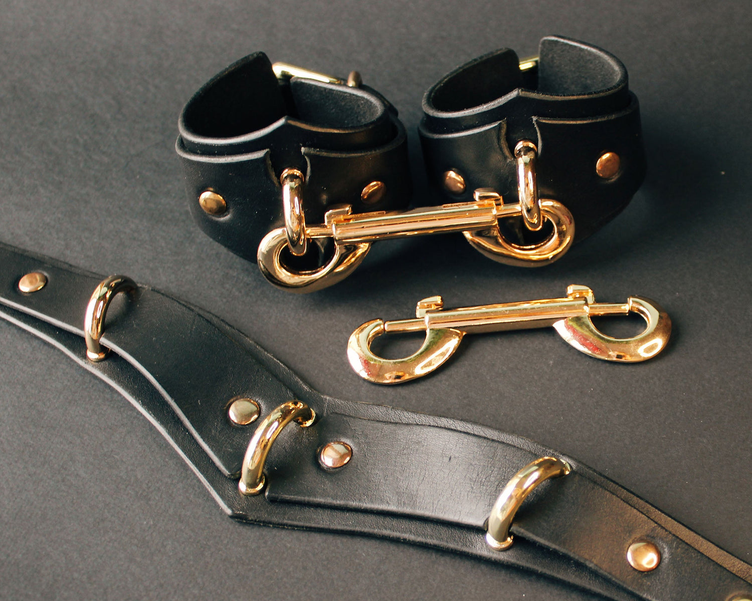 Black leather cuffs with gold hardware on a dark background