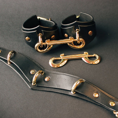 Black leather collar cuffs with gold hardware on a dark background