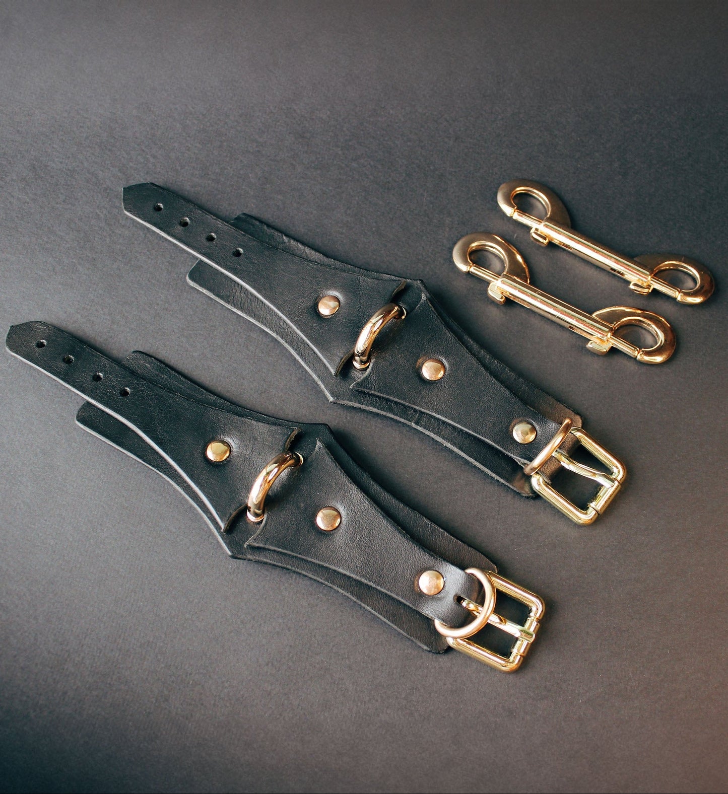 Black leather handcuffs  with gold buckles on a dark gray background