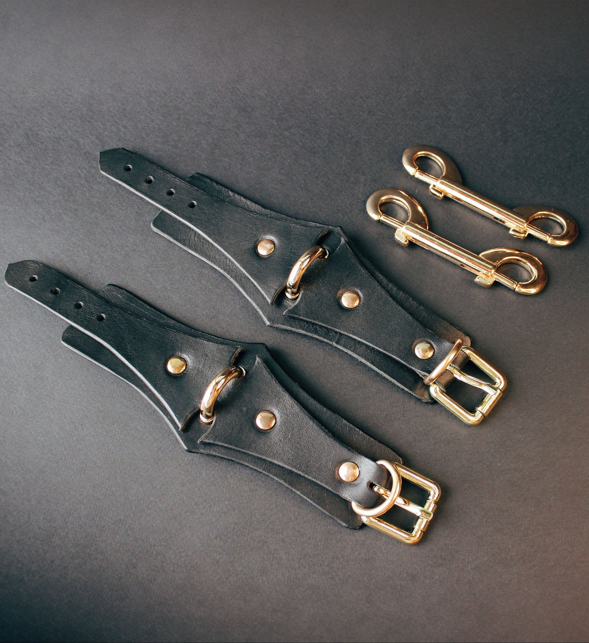 Black leather handcuffs  with gold buckles on a dark gray background
