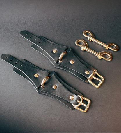 Black leather handcuffs  with gold buckles on a dark gray background