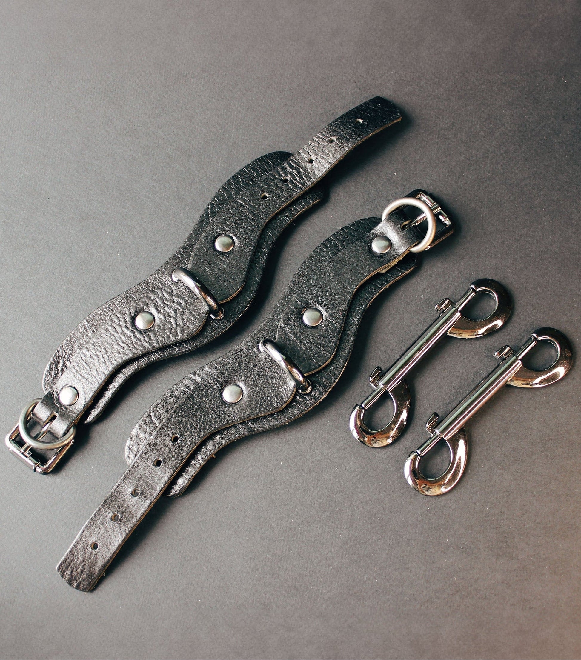 Two leather wrist cuffs with metal hooks on a gray background