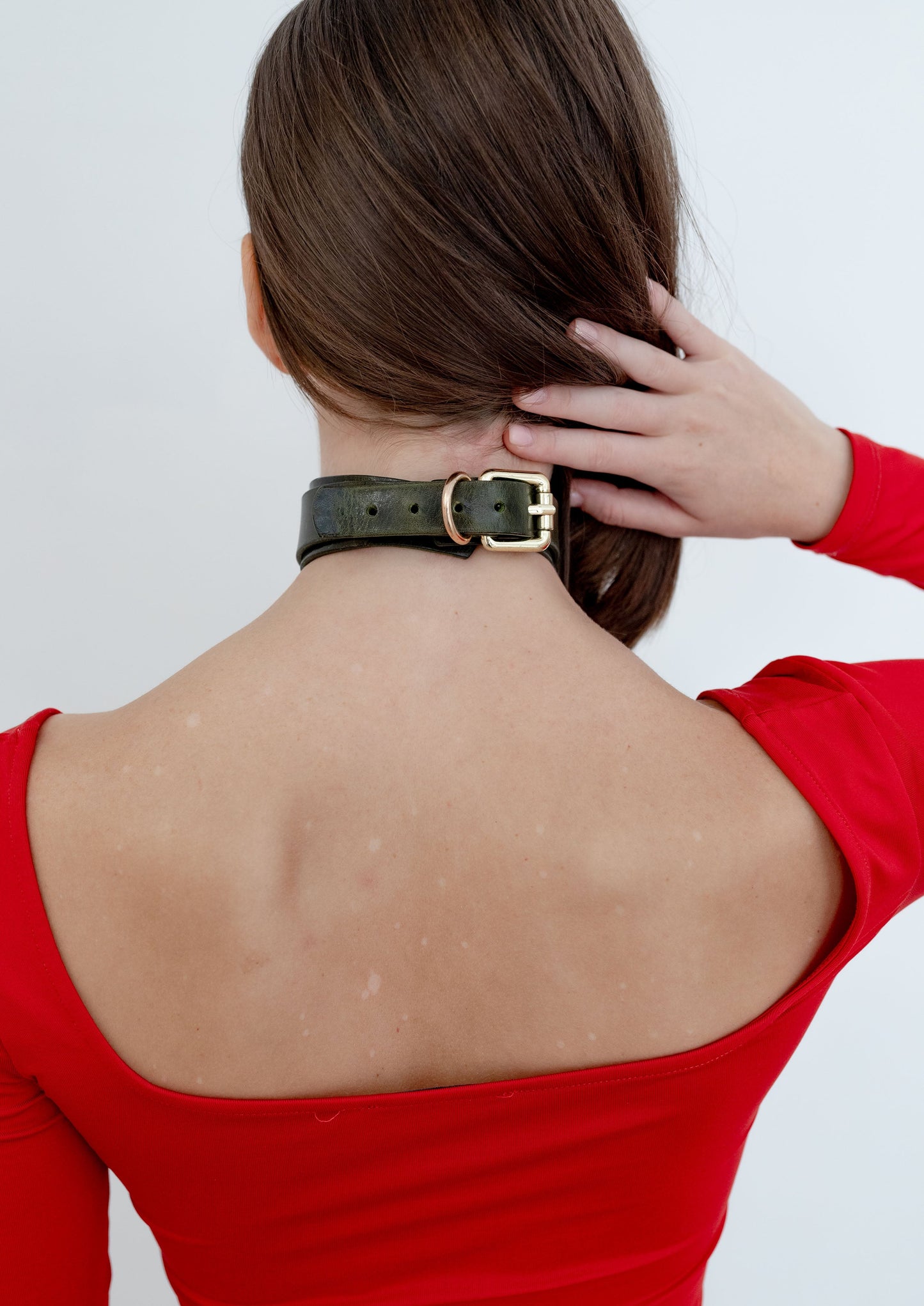 Person wearing a green leather choker with a gold hardware on a plain background