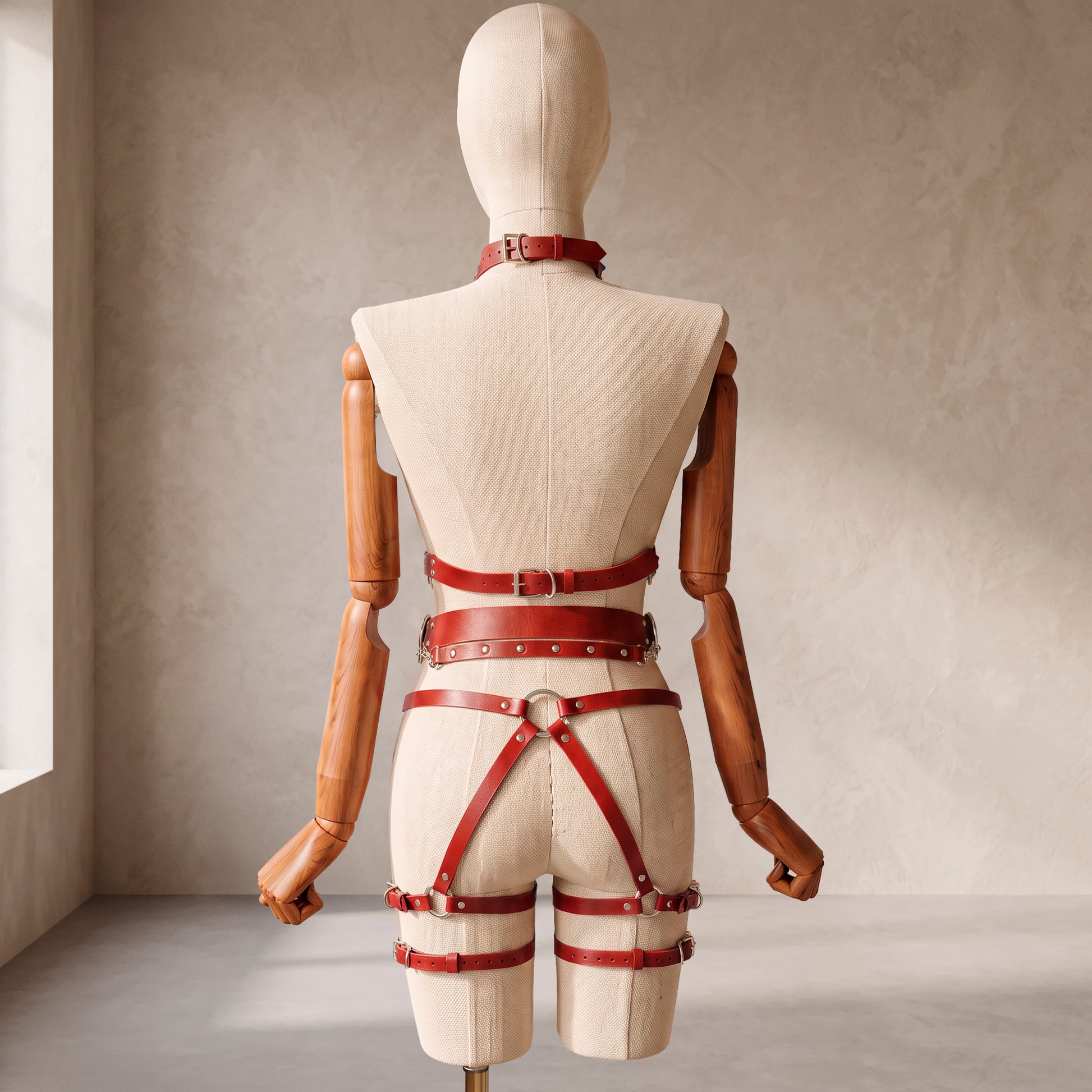 Back view of a deep red leather full body harness set with an open bust harness, open crotch garter belt, removable leather handle, large front ring, adjustable straps, and gold-tone metal hardware.