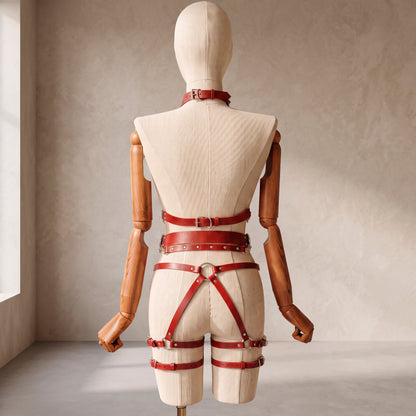 Back view of a deep red leather full body harness set with an open bust harness, open crotch garter belt, removable leather handle, large front ring, adjustable straps, and gold-tone metal hardware.